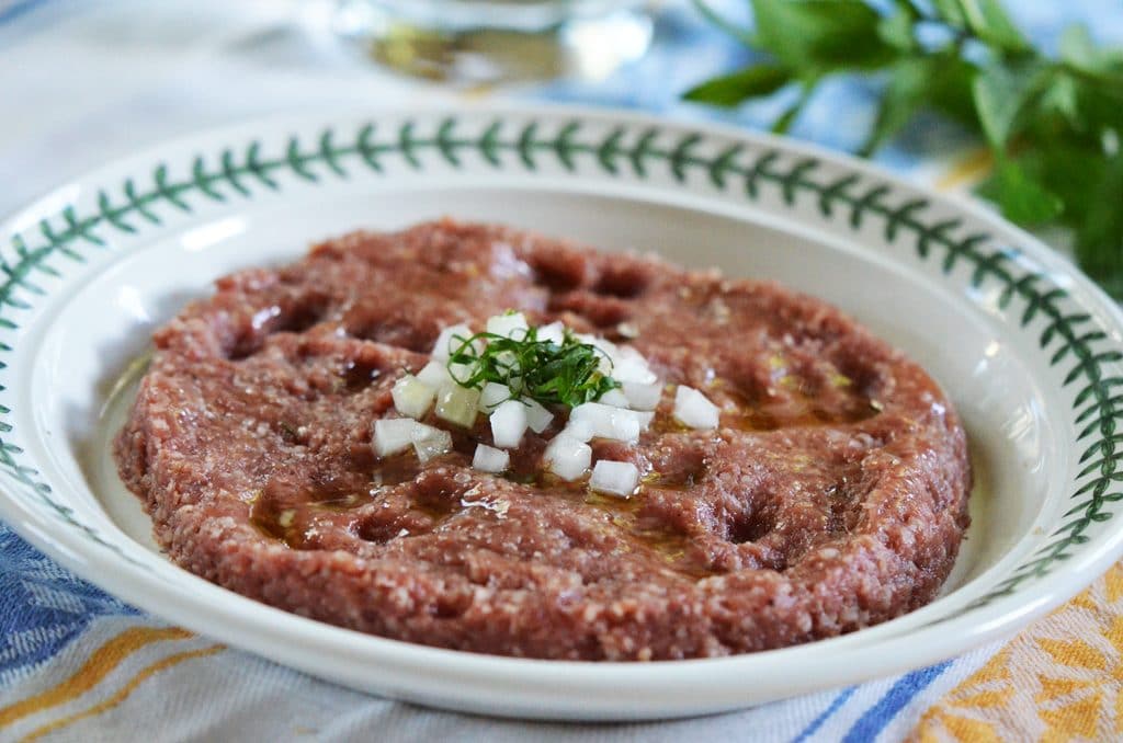 Kibbeh Nayeh, raw ground meat with bulgur, onion, and spices on a plate with mint, MaureenAbood.com