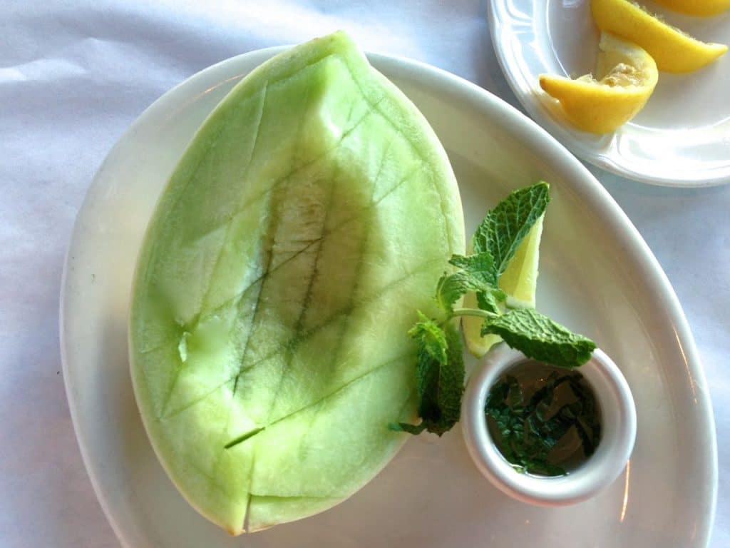 Ripe honeydew melon with a cup of fresh mint syrup and lemon wedges, on a white plate, Maureen Abood.com