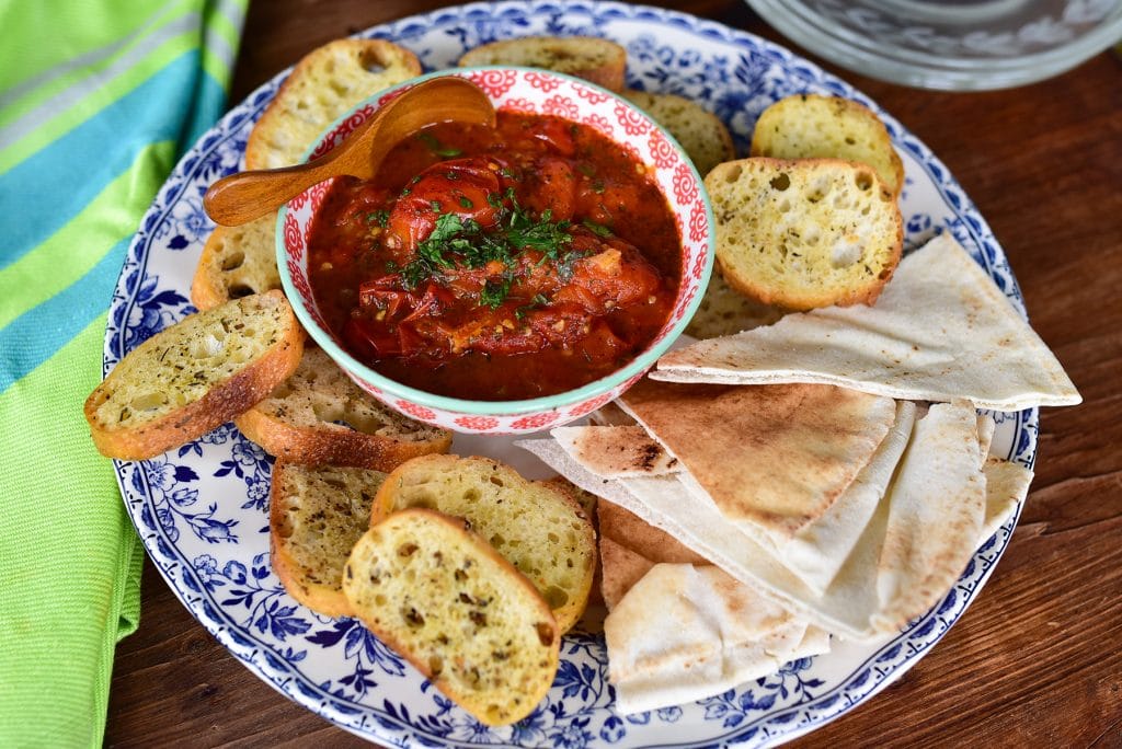 Tomato salsa topped with fresh mint in a bowl, surrounded by pita bread on a platter