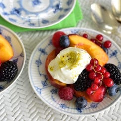 Fresh summer fruit with Lebanese ashta cream on a blue and white plate, surrounded by a wicker table and silver spoons from Maureen Abood
