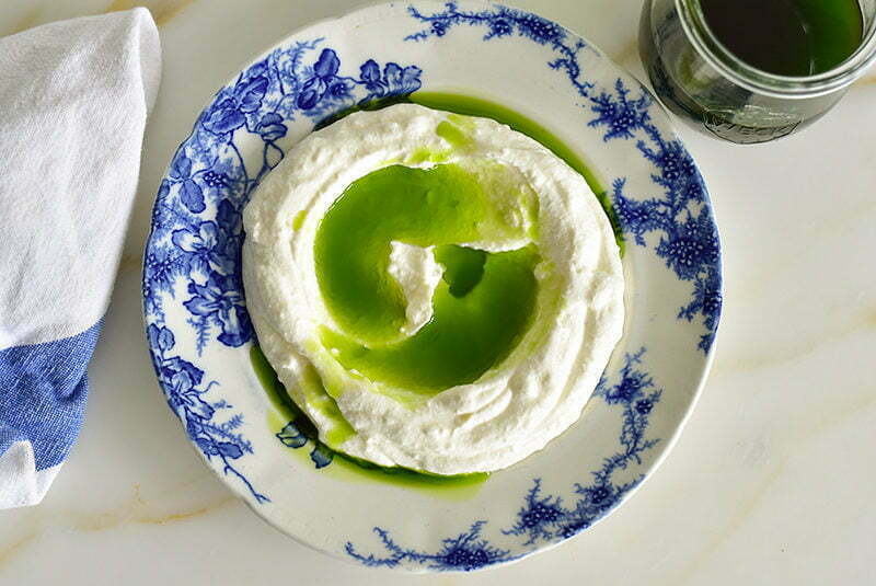 Basil oil poured over labneh in a blue dish