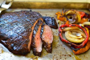 Grilled flank steak slices on a sheet pan with grilled peppers