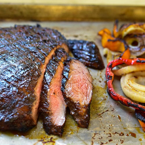 Grilled flank steak slices on a sheet pan with grilled peppers