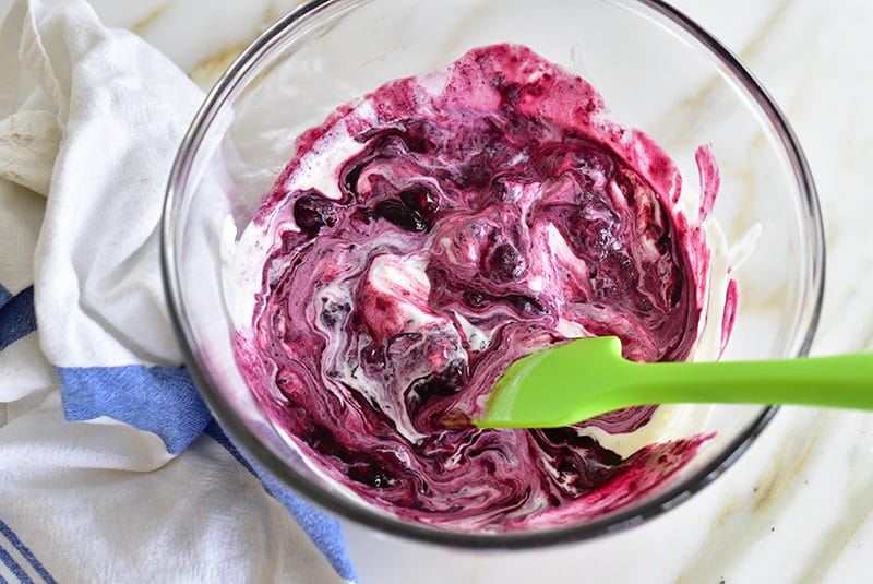 Labneh stirred with blueberry sauce in a bowl with a green spatula
