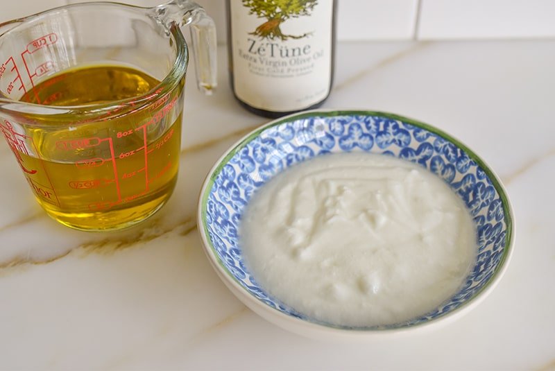 Olive oil in a measuring cup on the counter with a bowl of yogurt