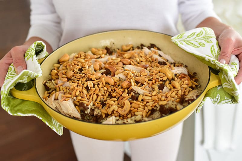 Rice pilaf with nuts in a yellow dish held by two hands