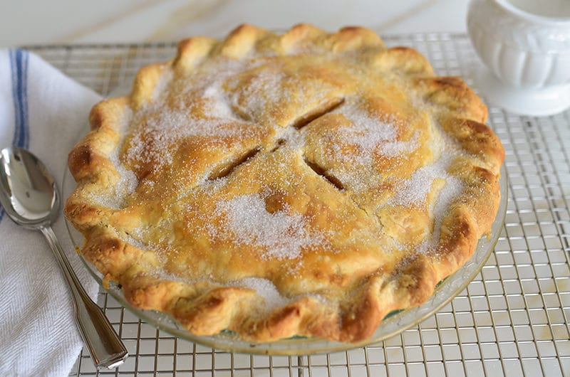 Apple pie on a rack with sugar and spoon