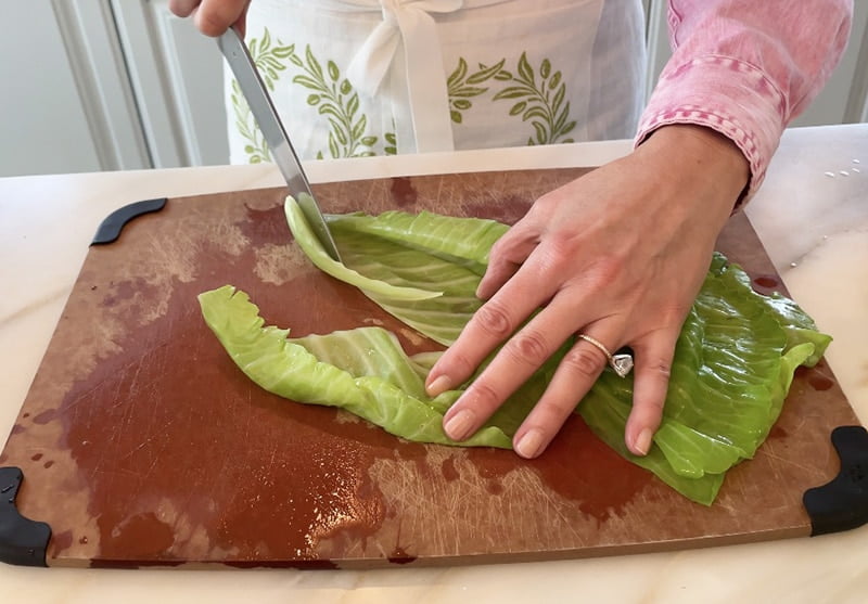Center rib being cut out of a cabbage leaf on a cutting board