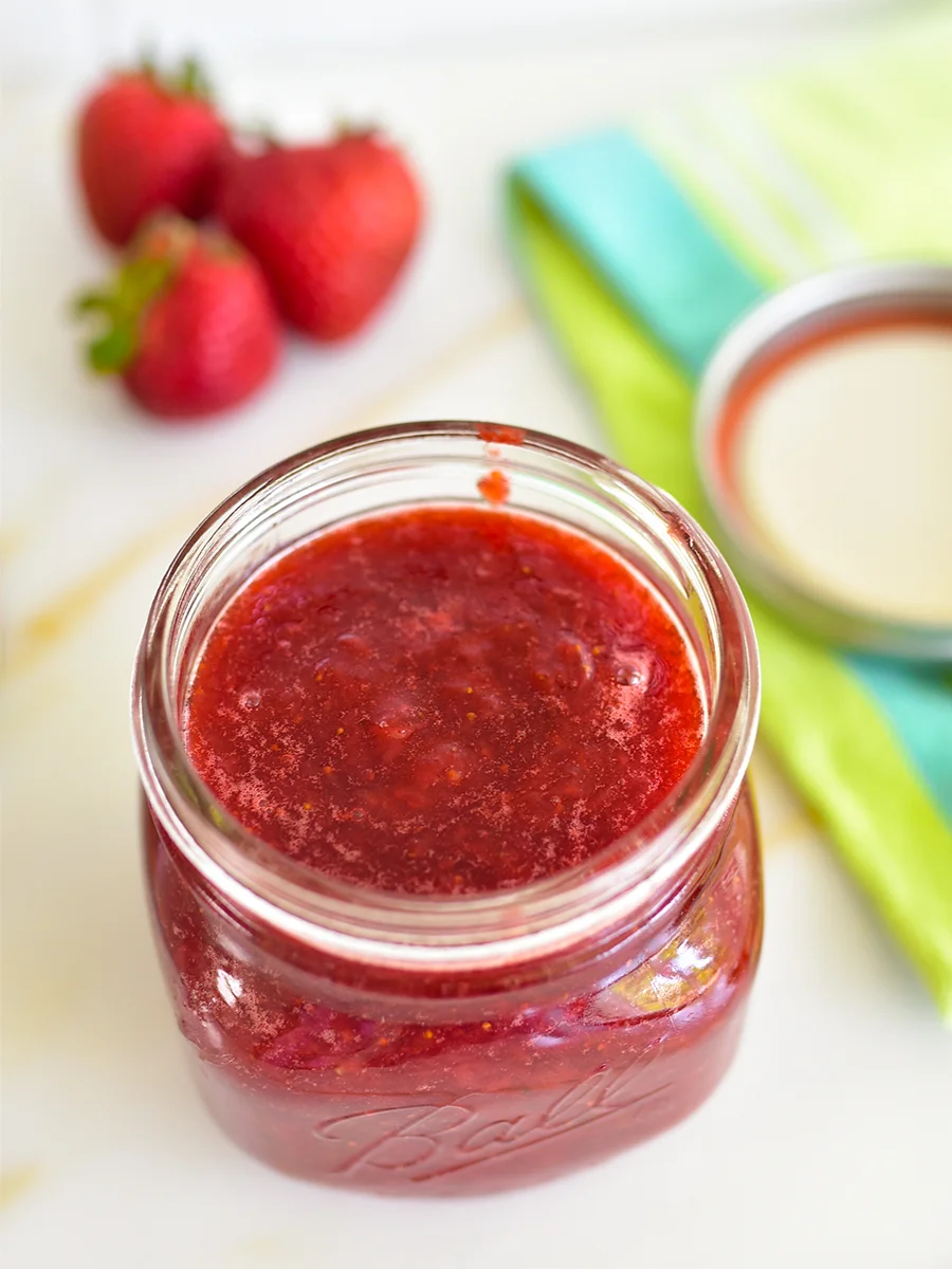 Red strawberry jam in a jar with berries in the background