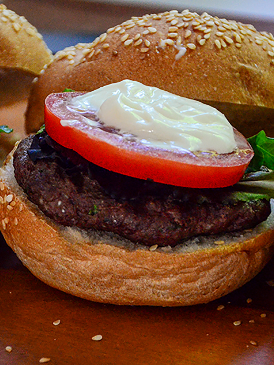 Lamb hamburger with a slice of tomato, mayonnaise, and bun top on the side